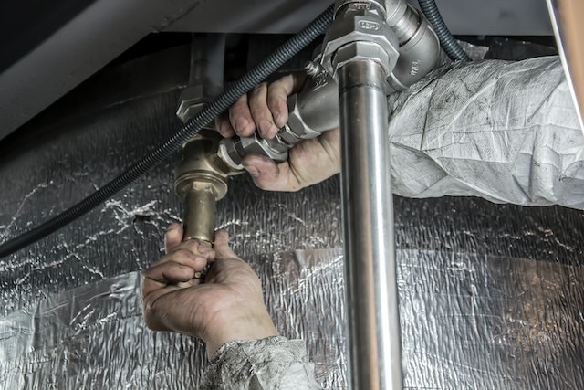 Close up of someone's arms fixing a pipe under a sink